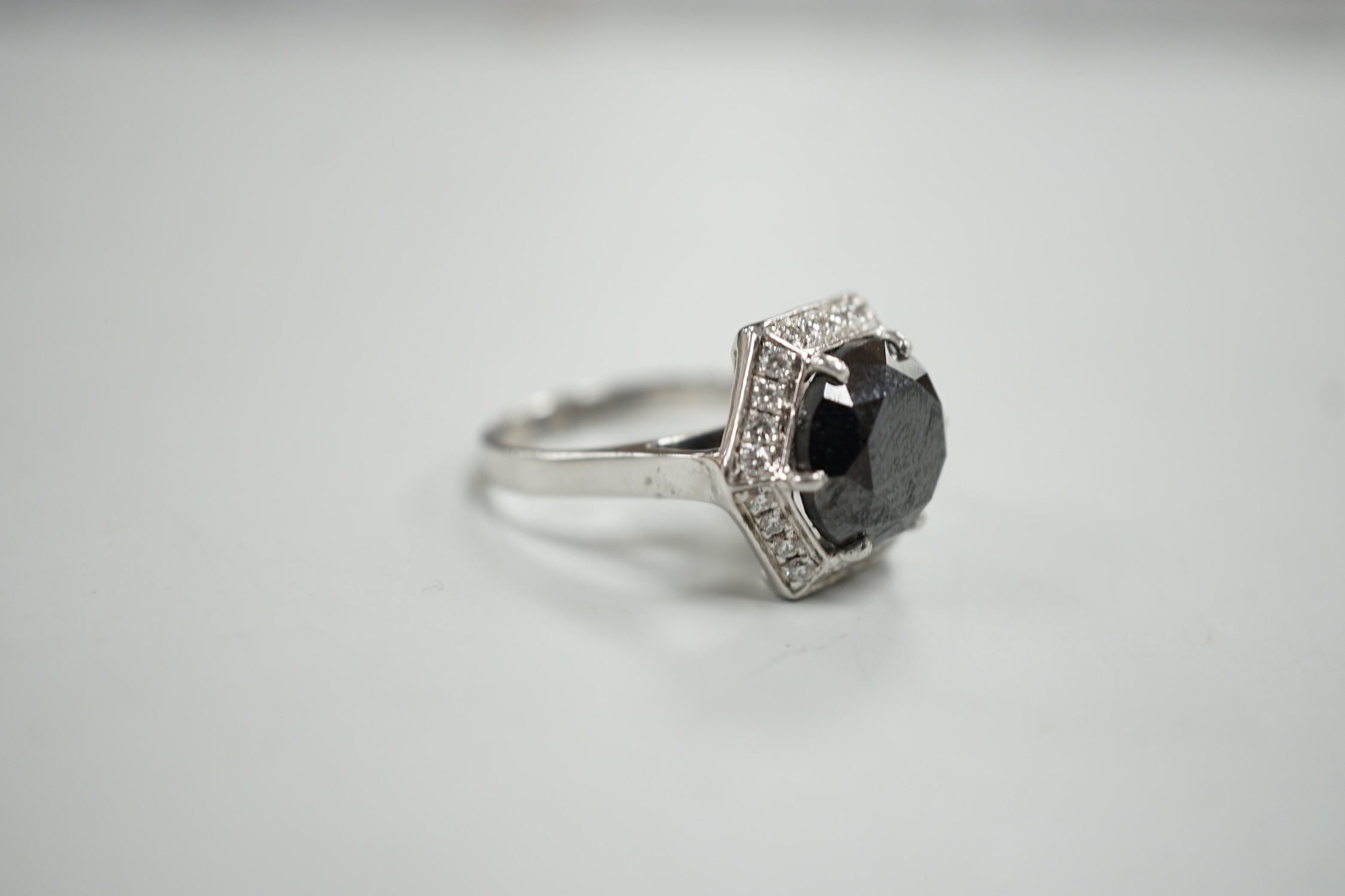 A modern 750 white metal and hexagonal cut black diamond set dress ring, with diamond chip set border, size N/O, gross weight 7.8 grams.